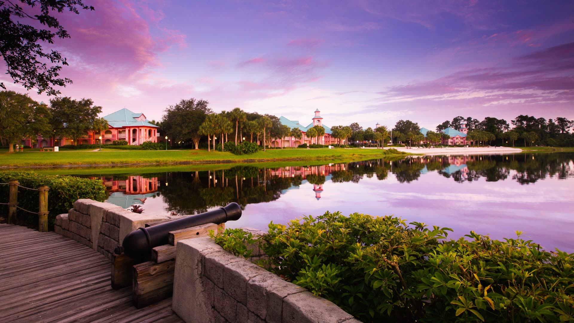 Tropical resort at sunset with palm trees and a dock overlooking a lake